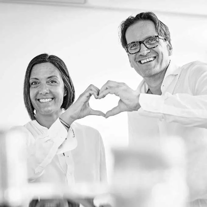 Kieferorthopädin Sabine Ritter und Kieferorthopäde Jens Ritter stehen nebeneinander und formen mit ihren Fingern ein Herz