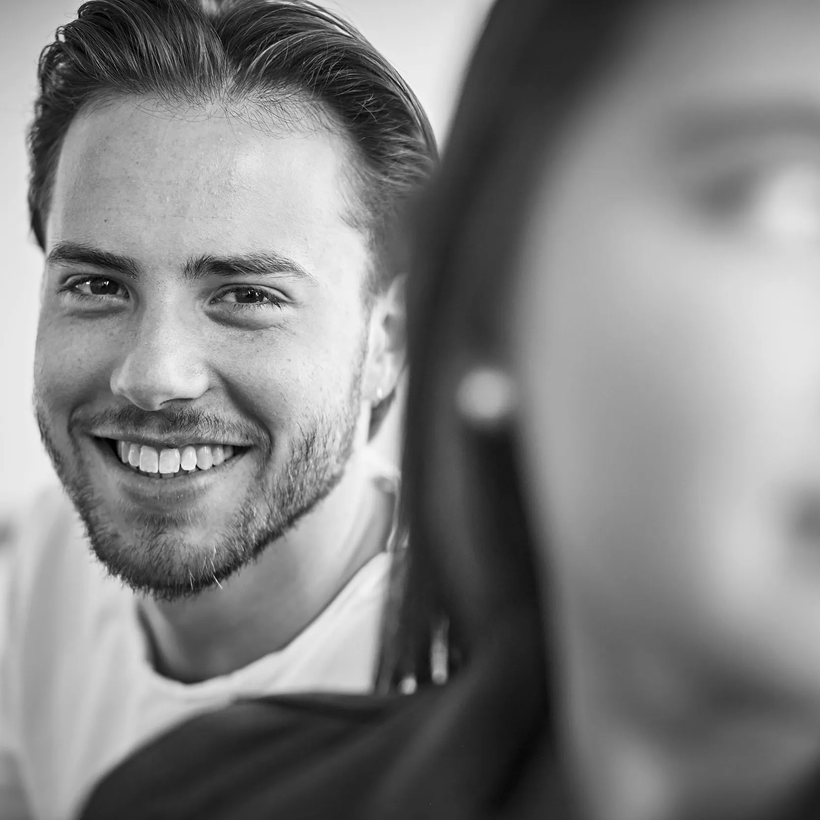 Junger Mann schaut lächelnend mit schönen Zähnen hinter Mädchen hervor